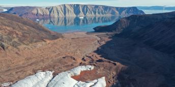 A beautiful view of Greenland showing a small patch of snow in the foreground against a backdrop of greenery, with a lake in the background