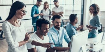 Three adults watching and pointing at a computer and smiling.