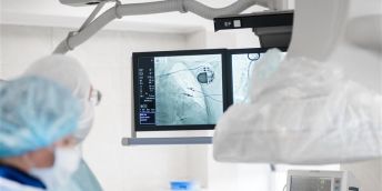 A cardiac surgeon in the operating room observes on x-ray monitors a pacemaker installed in a patient.