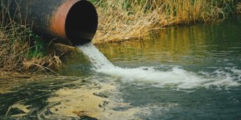 Water pours into river from rusty pipe
