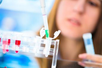 A scientist with long brown hair drops a solution from a pipette, in a laboratory.