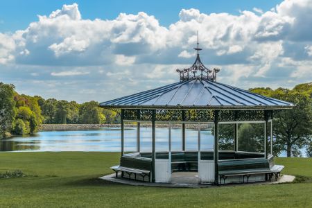 A bandstand by a lake in a lush green park.