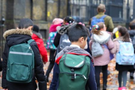 Young children walking to school, wearing coats and backpacks.