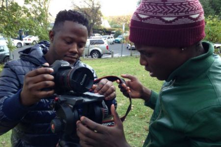 Two young people, one holding an SLR camera. They are both examining it.