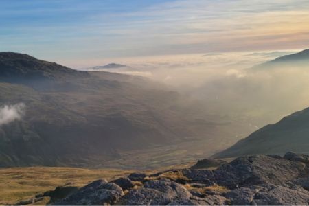 Mist on top of rolling hills in the Duddon Valley, a rugged landscape with mountains and rocks.