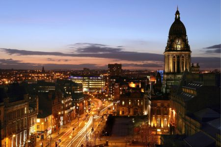 Leeds city centre at night, with the Town Hall clock tower, office buildings with lit up windows and traffic on the streets.