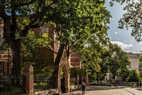 A person walks down the path outside the Great Hall on a sunny day.