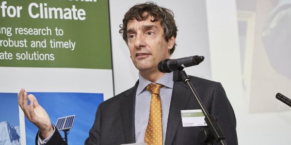 A head and shoulders shot of Professor Piers Forster stood behind a microphone on a stand.