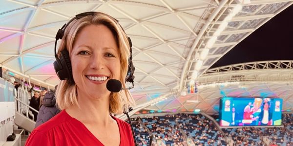 Jacqui Oatley at a sports event in a stadium full of people, wearing a commentator headset.