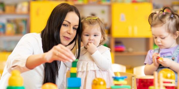 A nursery worker plays with children in a room full of colourful toys