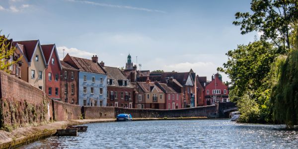 The River Wensum in Norwich in daytime. Colourful houses line the river banks.