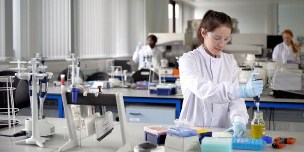 A young woman in a lab coat is holding a pipette and concentrating on moving liquids for a scientific experiment.
