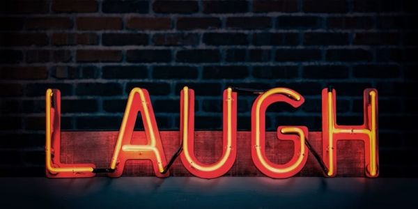 An illuminated sign that says 'laugh' on a dark brick wall