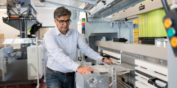 A person operates a large white weaving machine in the Spinning, Knitting and Weaving lab. Other textile equipment is in the background.