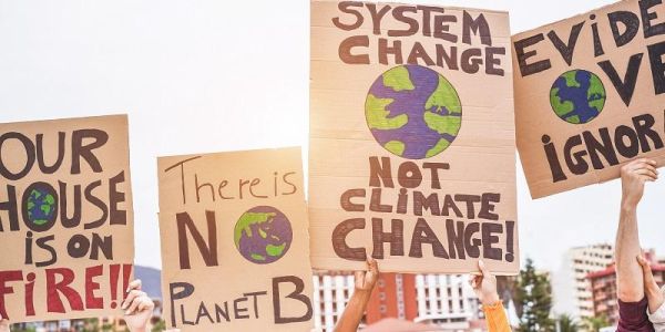 People protesting for action on climate change with signs that read 'Our house is on fire', 'There is no planet B' and 'System change not climate change'.