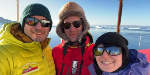 Will Homoky, Aly Lough and Chiara Krewer on the RRS Sir David Attenborough with icebergs in the distance behind them