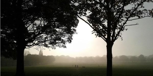 Image shows the early morning sun rising over Roundhay Park in Leeds with people walking in the distance