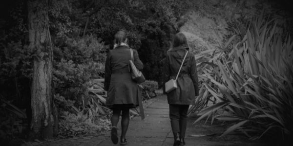 Two young women walk towards some shrubbery in a park