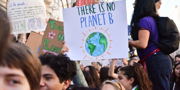 A crowd of people on a march against climate change. Several are holding placards. One says: There is no planet B.