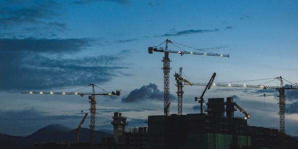 Several cranes on construction sites, sillhouetted against a dusk sky