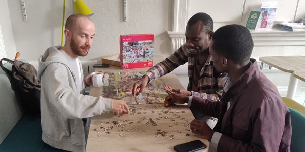Three men sit around a table completing a jigsaw