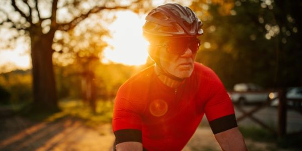 An older male cyclist riding on a road at sunset
