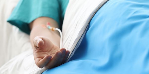 A hospital patient's arm with a fluid line going into it, laying over the covers of the hospital bed