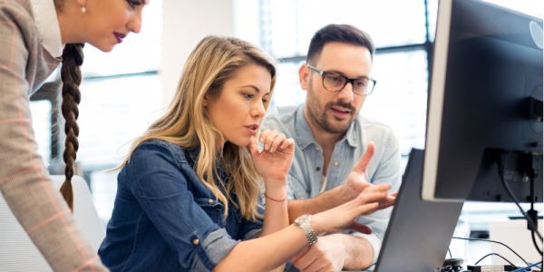 Three office workers sat in front of a desktop and PC screen.