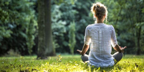 A person meditating in grassed woodland