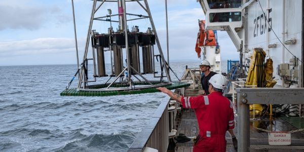 Crew lowering a scientific instrument into the sea from a research ship.