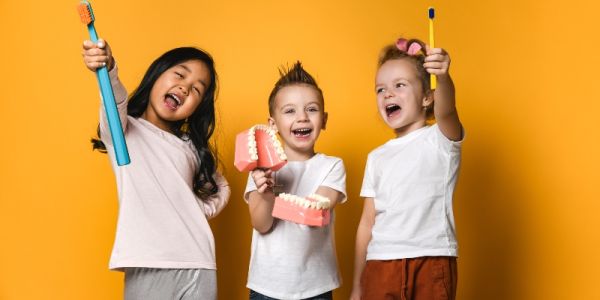 three children holding large toothbrushes and a model of teeth