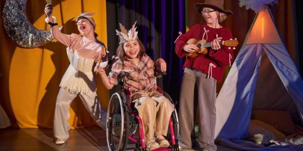 three young teenagers acting on stage. One of the young actors is a wheelchair user.