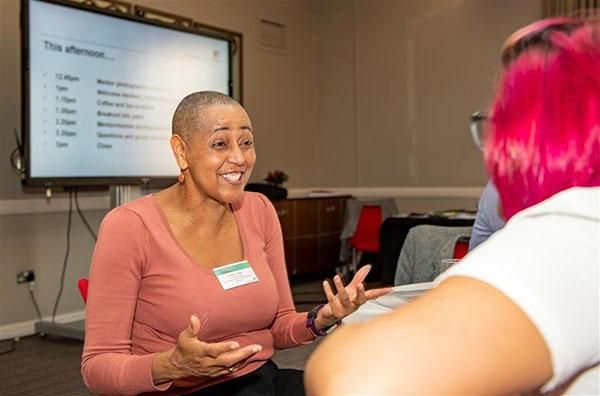 A person wearing a pink top and a name badge is standing in front of a smart board talking to a student