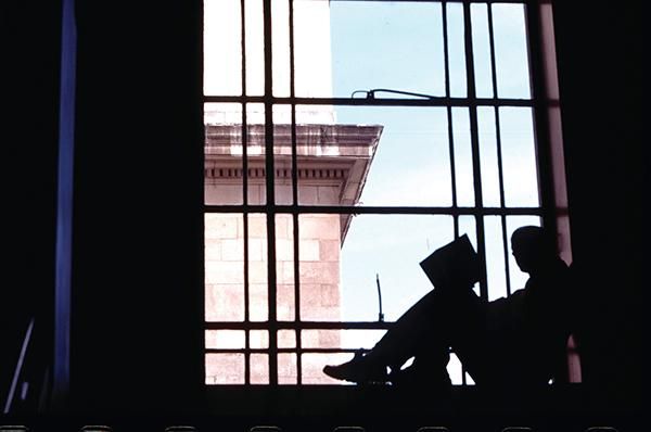 A silhouette of a person reading a book sat on a window sill