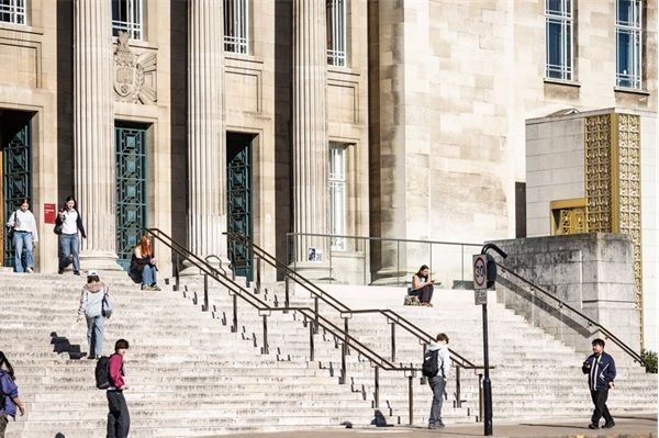 Students walking and sitting on the stone steps outside the Parkinson Building, with tall columns and architectural features in the background.