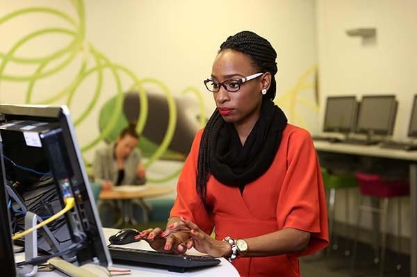 A student wearing a scarf and a red top working on a laptop.