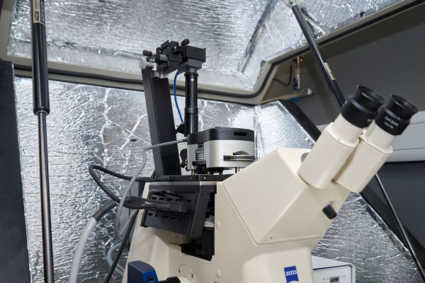 Close‑up view of the microscope inside a reflective, insulated enclosure showing a binocular eyepiece, camera or sensor mounted above the microscope body and mechanical positioning components.