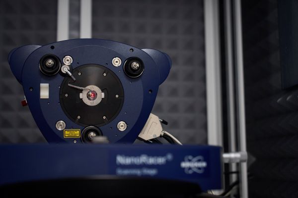 A close‑up of the blue instrument head mounted on a scanning stage, featuring a central circular aperture surrounded by small lenses, screws and calibration markers.