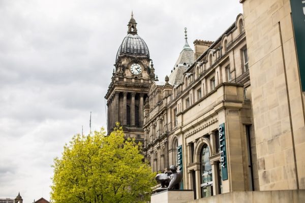 Wide landscape view of Leeds Town Hall clock tower taken at a slight angle and looking up. To the right of it is the front of the Library and Art Gallery.