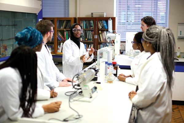 A postgraduate researcher demonstrates an experiment to a group of other postgraduate researchers inside the John Priestley Laboratory, School of Chemistry.