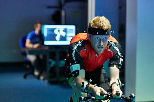 A person on a bicycle simulator, with another person monitoring their performance on a screen.