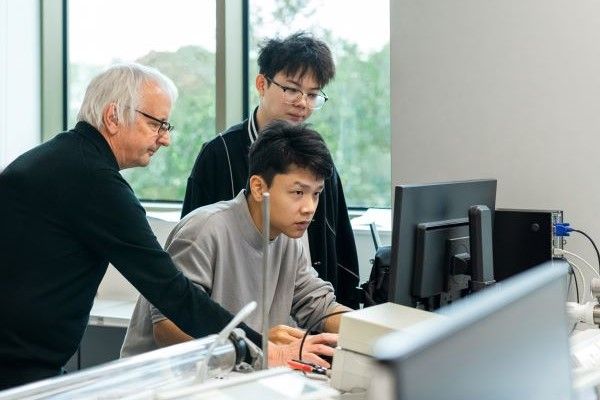 A tutor and students, leaning over and looking at a computer.