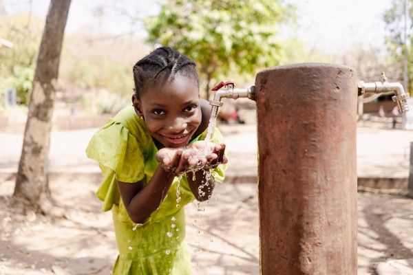 A smiling child drinks fresh water from a tap