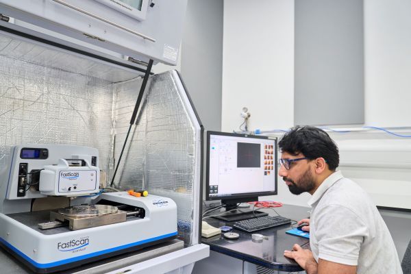 Bruker Dimension FastScan AFM machine housed in an insulated chamber, with someone sat to the right, looking at the machine whilstt using a mouse, attached to a computer running an on-screen research programme.