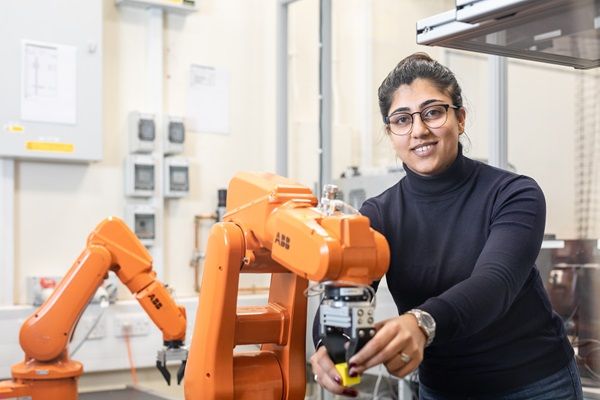 A student operating an industrial robot arm with a computer vision and conveyor belt system in the S C Loh Robotics Innovation Lab.