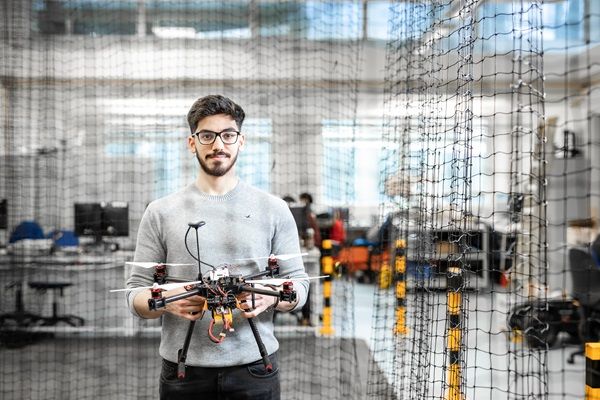 A student in a large lab, holding a drone