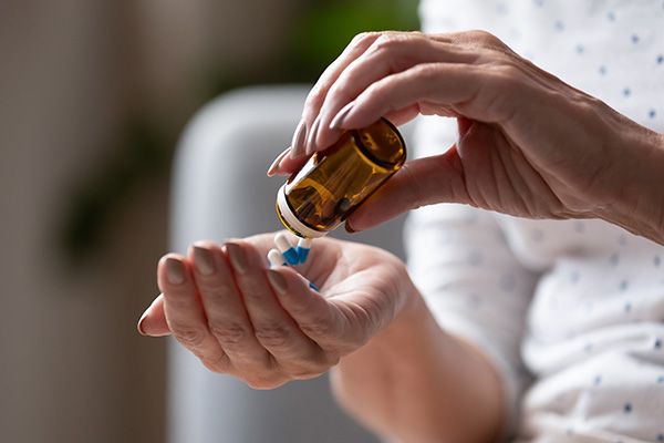 A close-up of a pair of hands. One hand is emptying a bottle of blue and white pill capsules into another, upturned open hand.