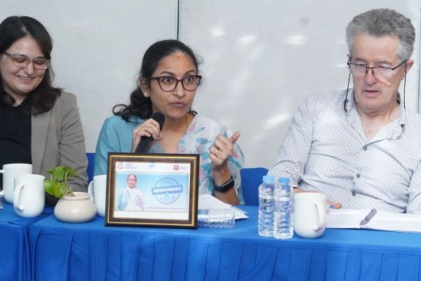 Dr Aarthi Bhuvaraghan (centre, holding microphone) and Professor John Walley seated at a table at a conference.