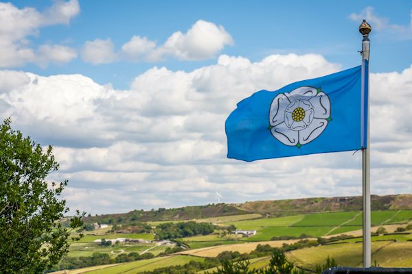 The Yorkshire Flag with a white rose against a blue background flies against a sunny sky with clouds over Yorkshire hills