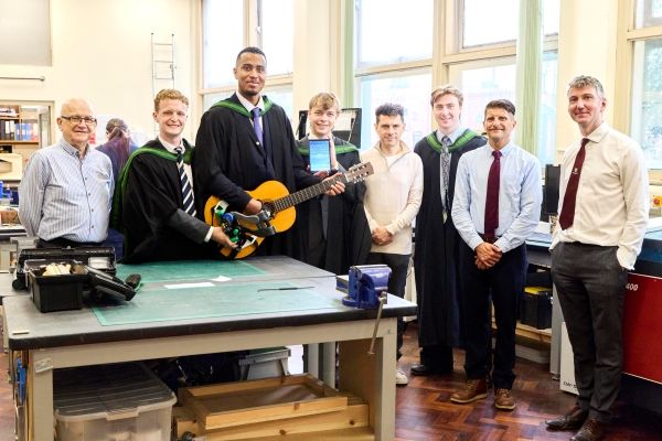 A group of graduates holding their guitar device which is fixed to the guitar with Alex Sobel MP, two professors and REMAP client.